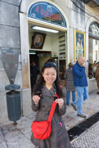 An essential travel guide to Lisbon includes trying the local drinks. Me holding two shot glasses of Ginjinha in front of A Ginjinha Bar on my first trip to Lisbon. 