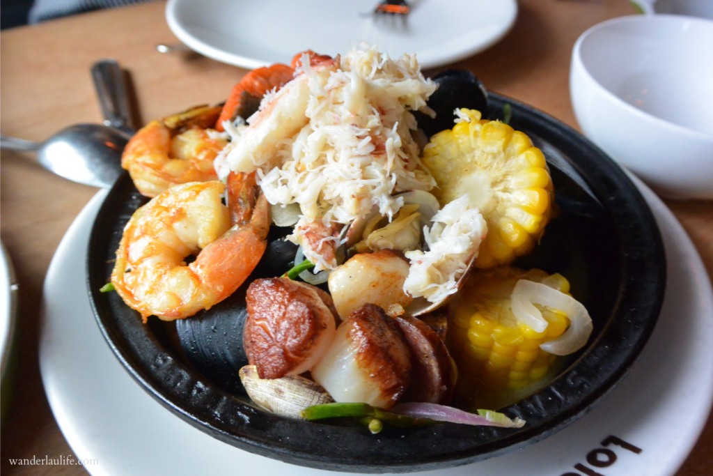 A hot skillet filled with scallops, crab meat, mussels, shrimp, and corn on the cob.