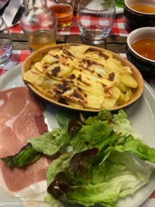 A warm tartiflette, a fresh green side salad, and a slice of prosciutto.