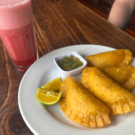 4 fresh empanadas with a side of salsa and cut limes with a tall glass of fresh juice from Bogotá.