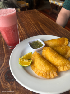4 fresh empanadas with a side of salsa and cut limes with a tall glass of fresh juice from Bogotá.